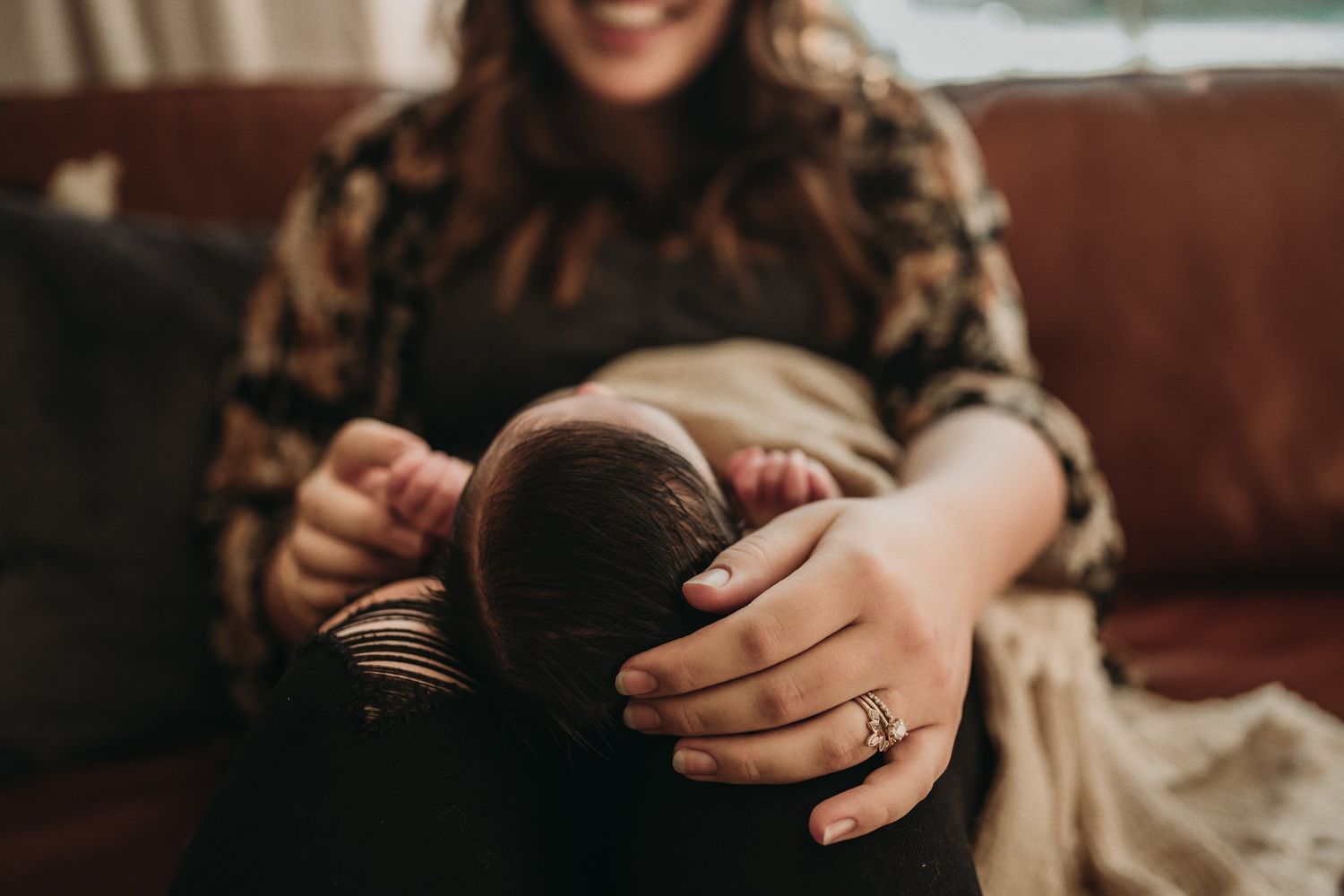 Candid moment of caregiver cradling sleeping infant on brown leather couch.