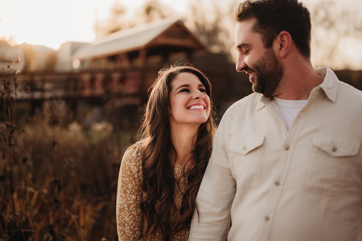 Candid outdoor portrait of a couple laughing together with warm sunset lighting.