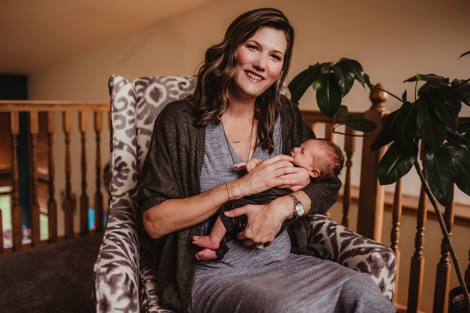 A relaxed portrait shows a parent cradling a newborn while seated in a patterned armchair.