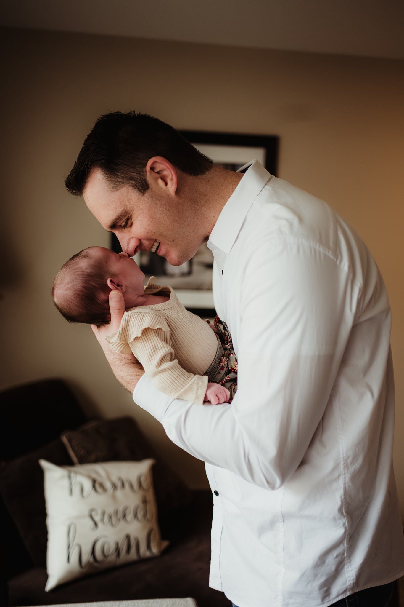 Parent in white shirt holding and smiling at newborn baby in living room.
