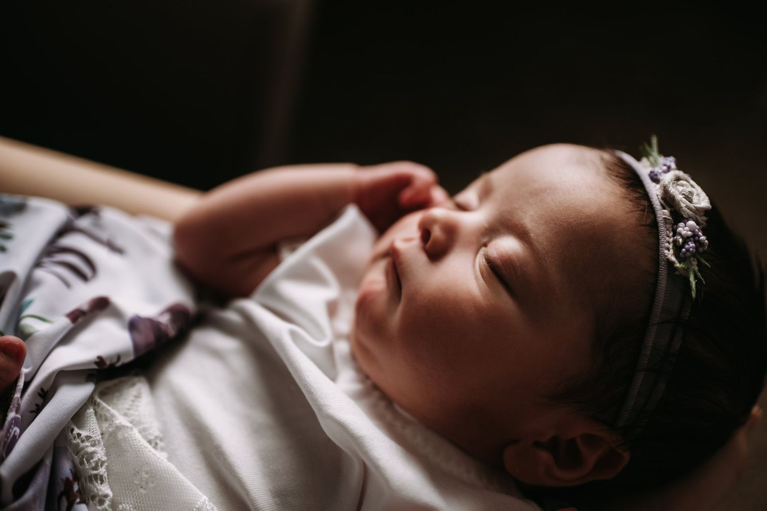 Close up of sleeping infant wearing delicate crown and white outfit in soft lighting.