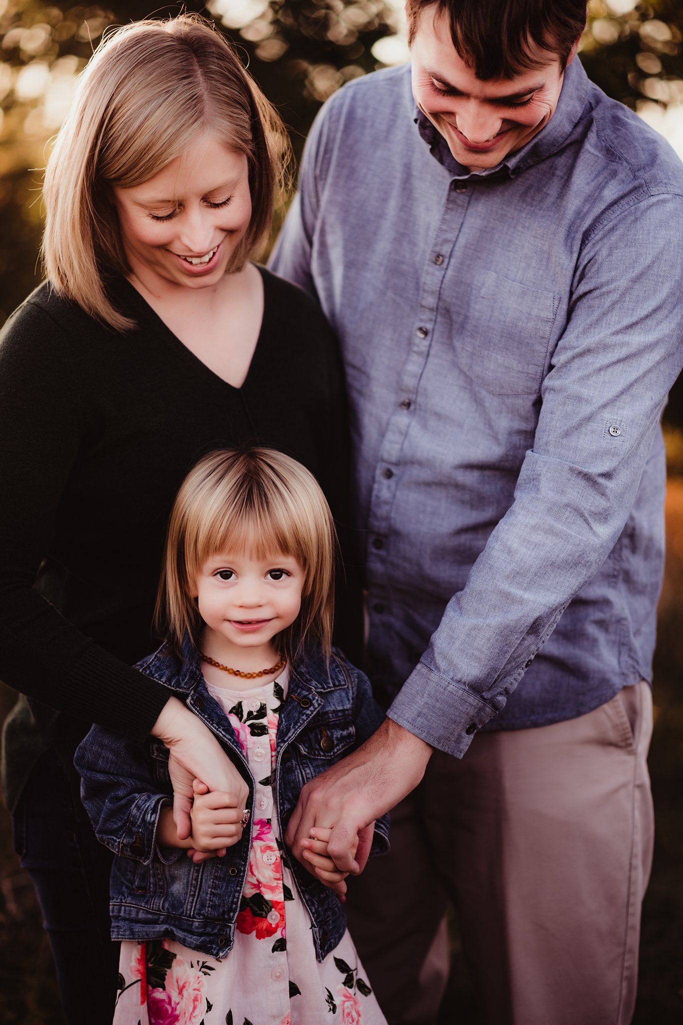 Intimate family portrait with casual clothing against natural outdoor backdrop.
