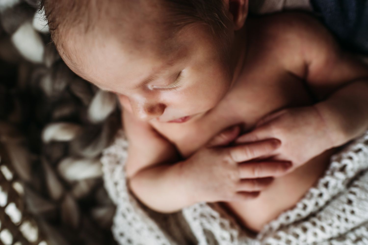 Intimate close-up of a sleeping newborn wrapped in soft knitted fabric.