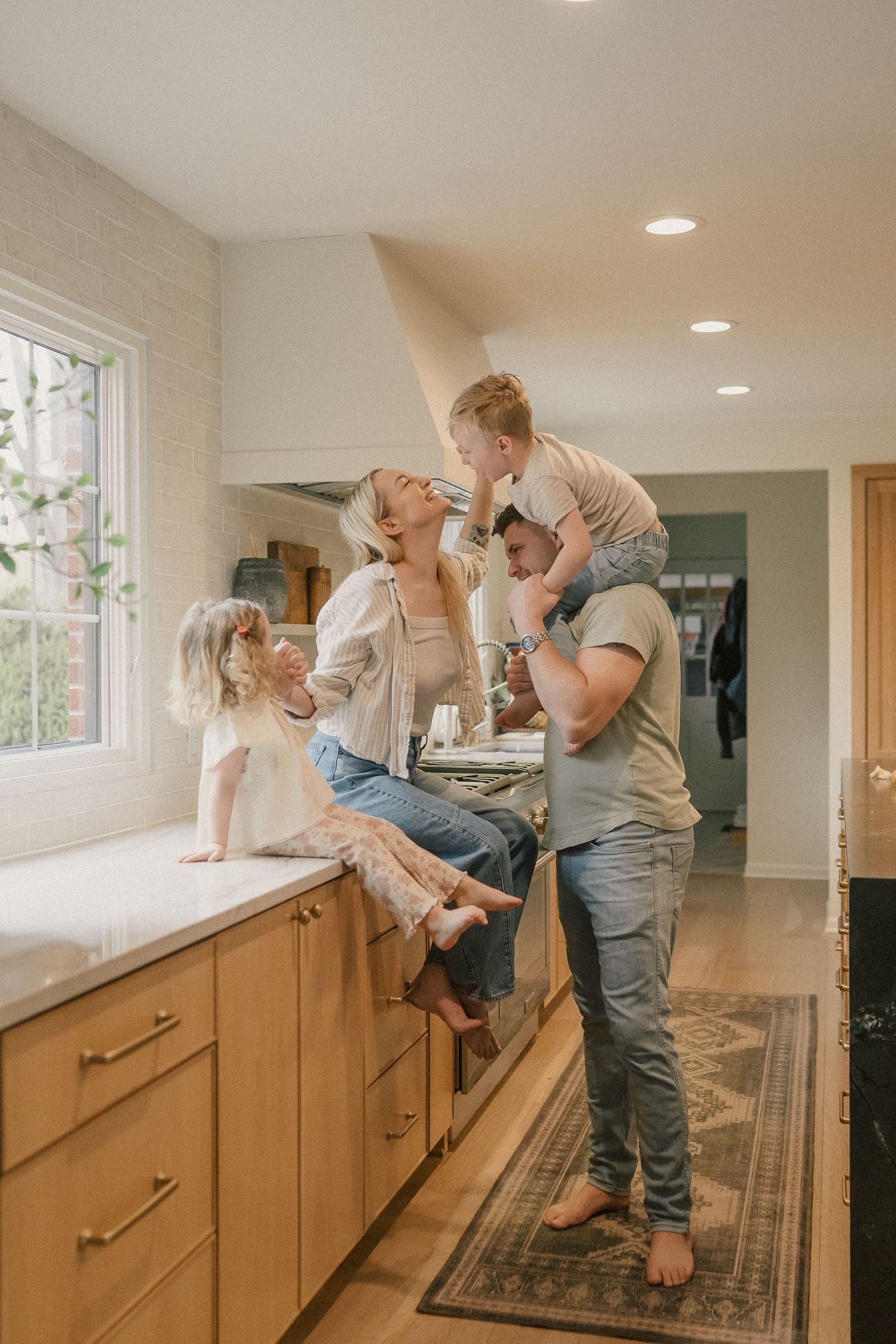 Happy family of four laughing together in bright modern kitchen.