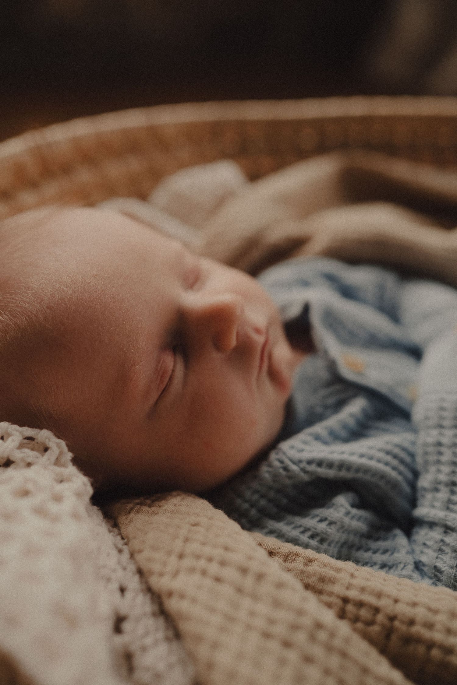 Sleeping newborn baby wrapped in a soft blue knit blanket nestled in a wicker Moses basket.