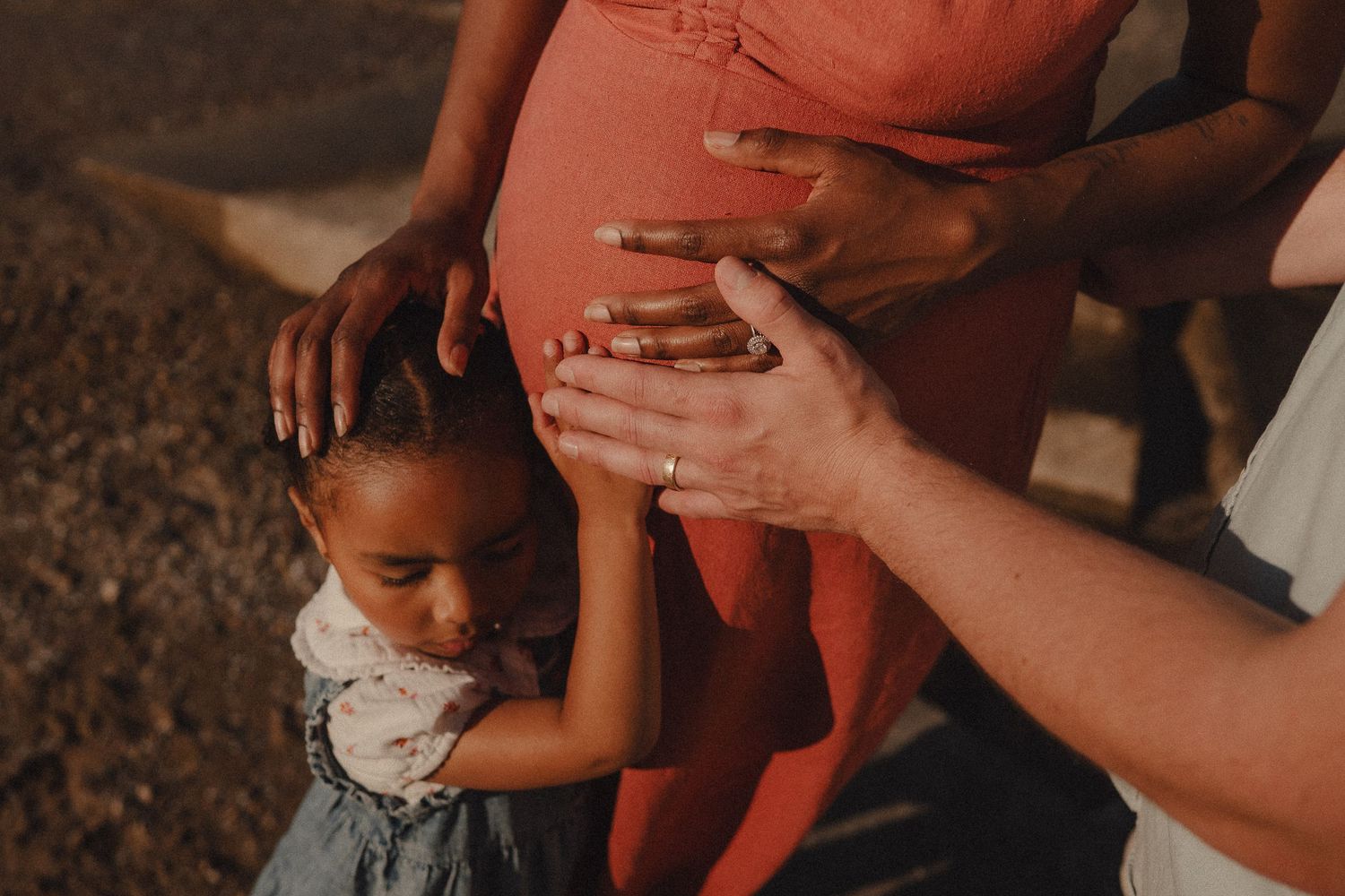 Young girl touching pregnant woman's belly in a warm outdoor maternity photo session.