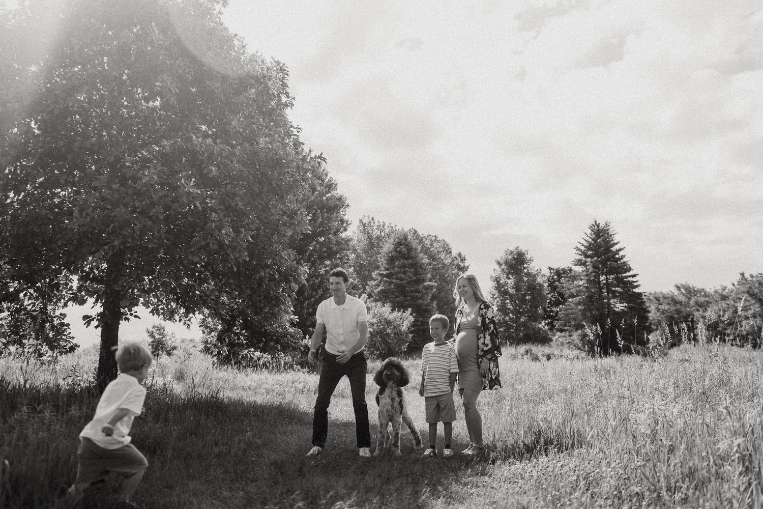 Black and white photo of a family with children playing outdoors in a grassy field near trees on a sunny day.