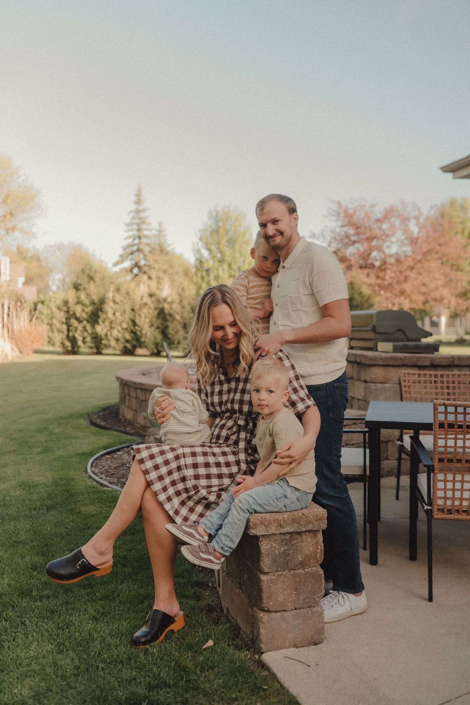 A happy family of four poses together on a stone patio surrounded by colorful autumn trees at sunset.
