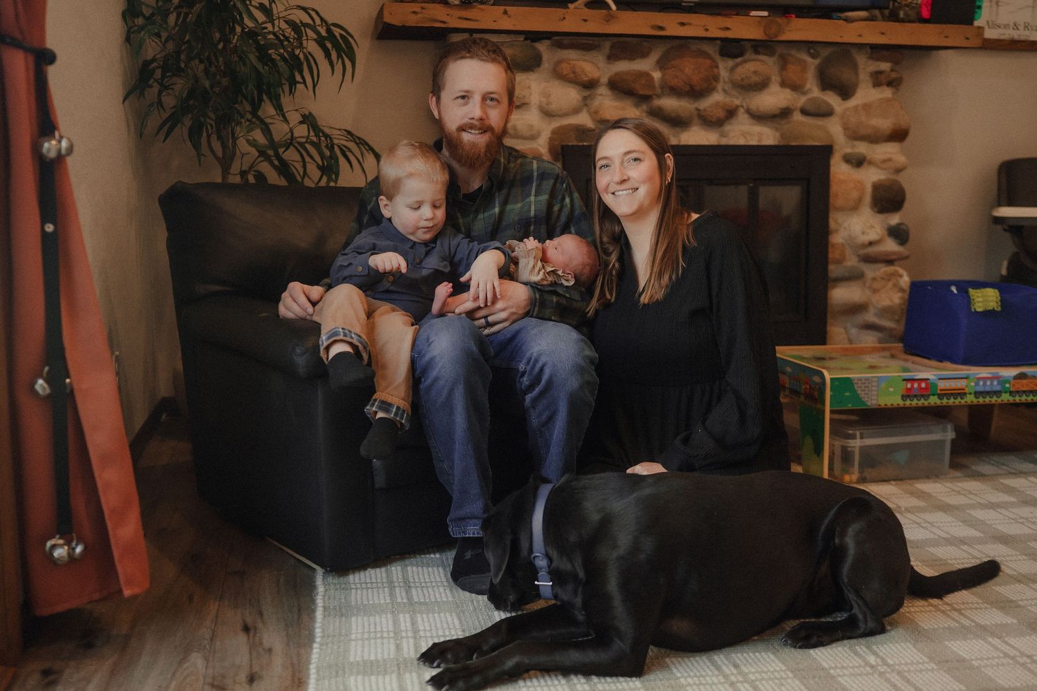 A family sits together on a comfortable couch in a cozy living room with stone walls and wooden accents.