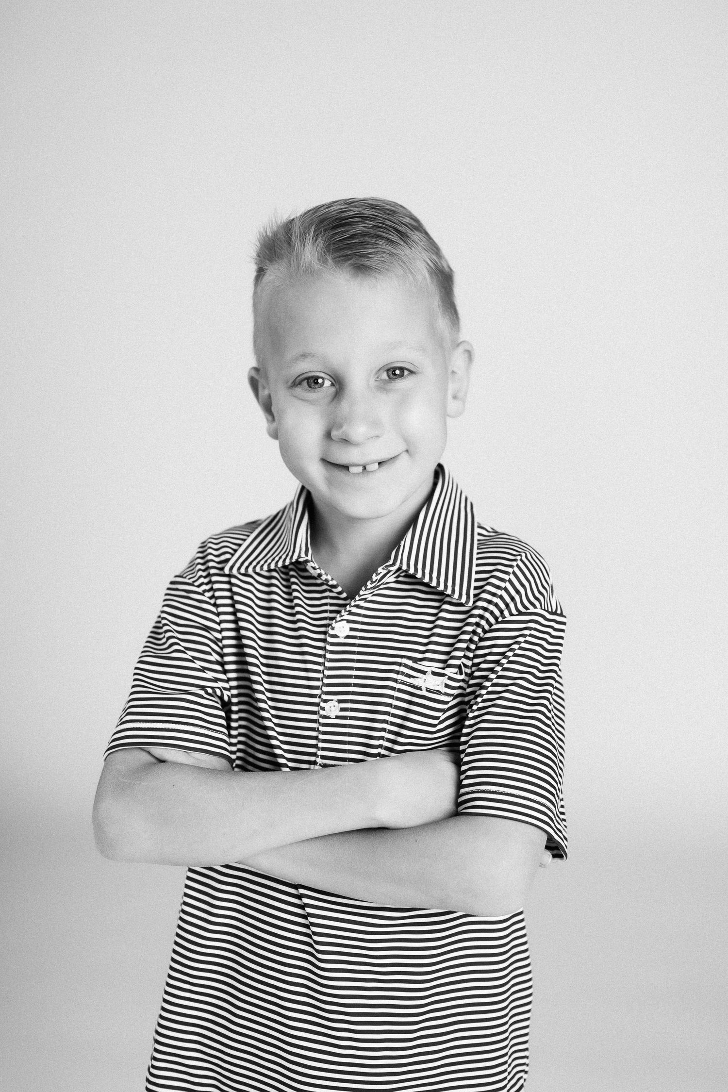 A series of black and white studio portraits showing a child in a striped polo shirt with different expressions.