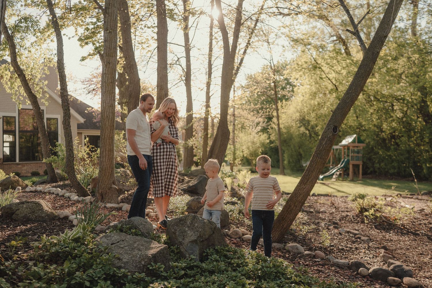 Family of four enjoying a sunny outdoor garden with lush trees and natural landscaping in a backyard setting.