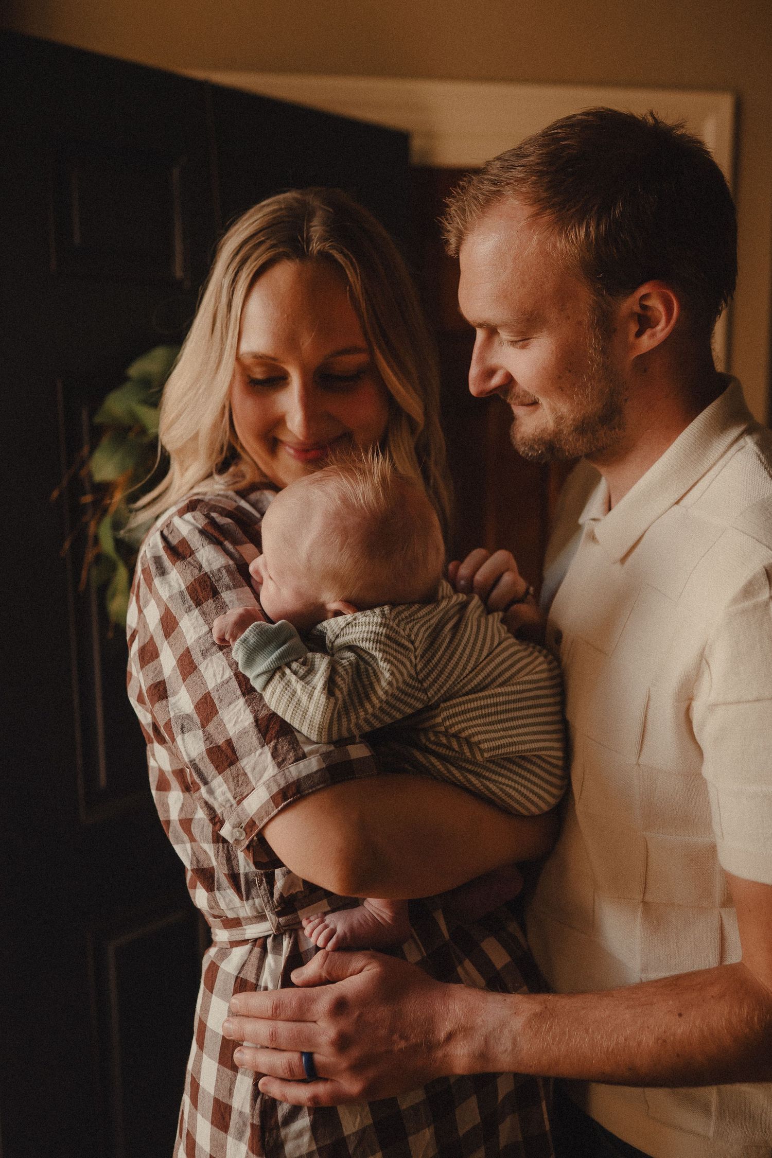 A couple gazes lovingly at their newborn baby in a warmly lit indoor setting.