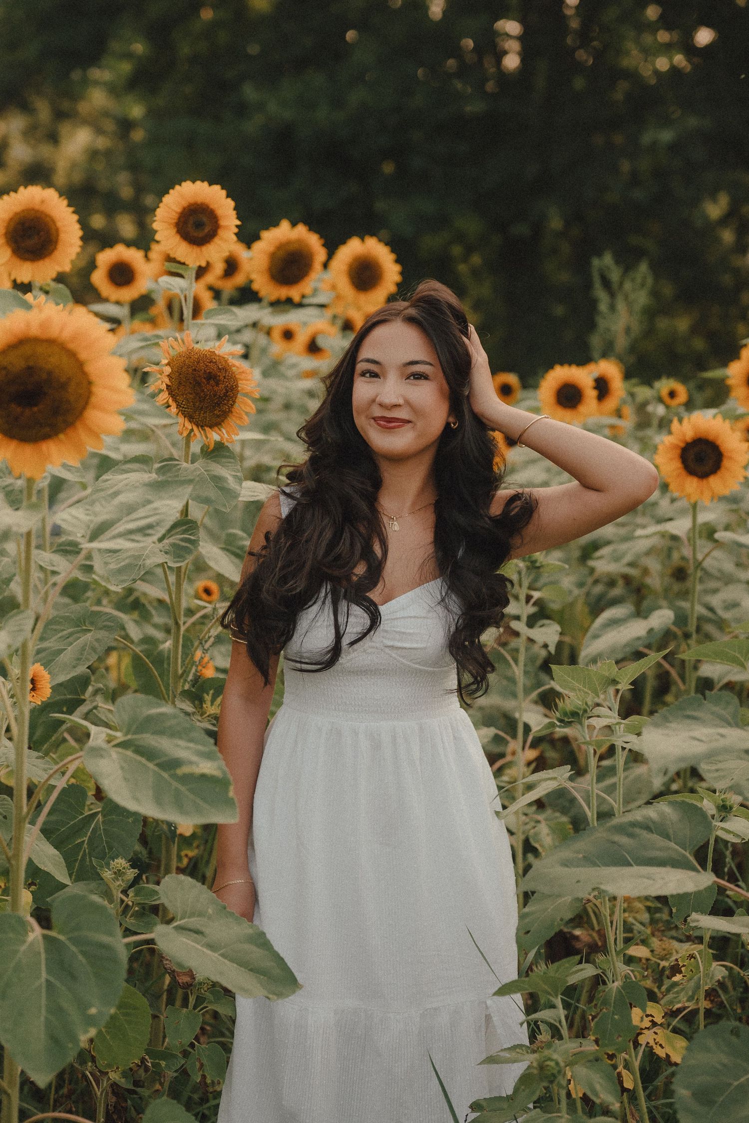 Young woman in white dress posing gracefully among tall sunflowers in a field.