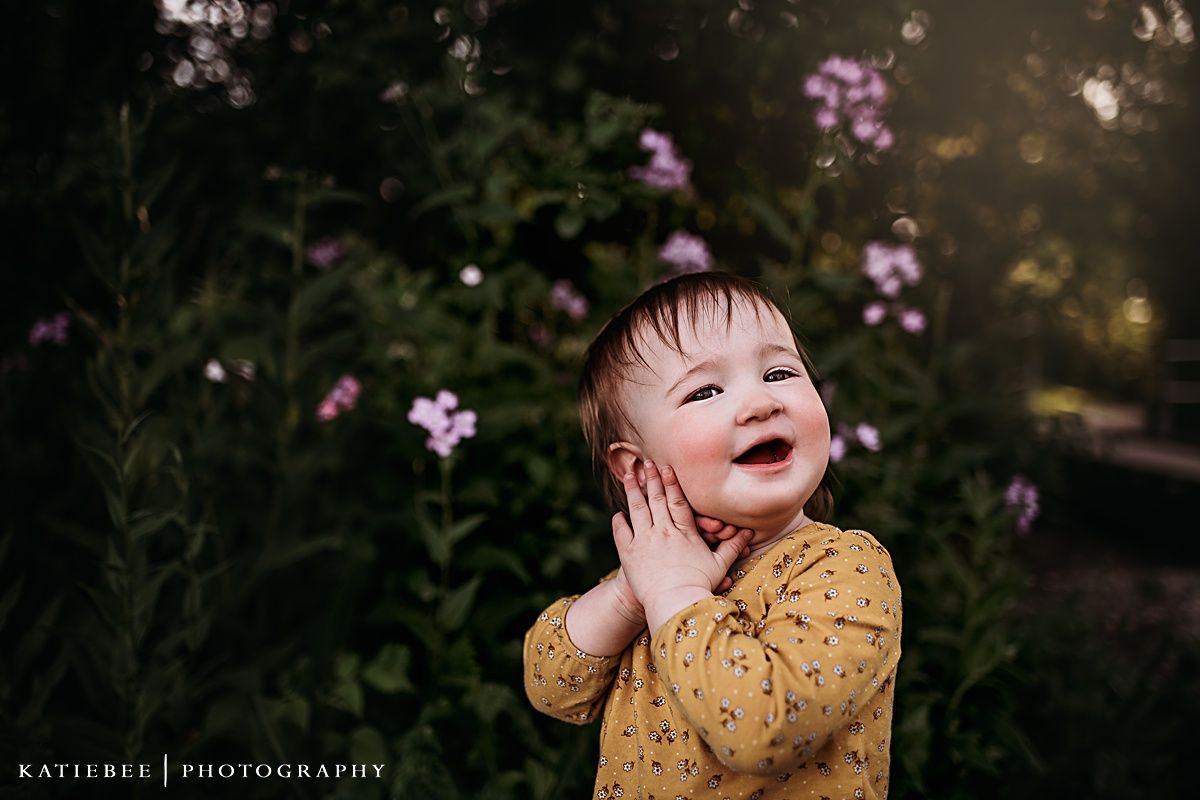 Joyful expression captured against blurred purple flowers and sunset backdrop.