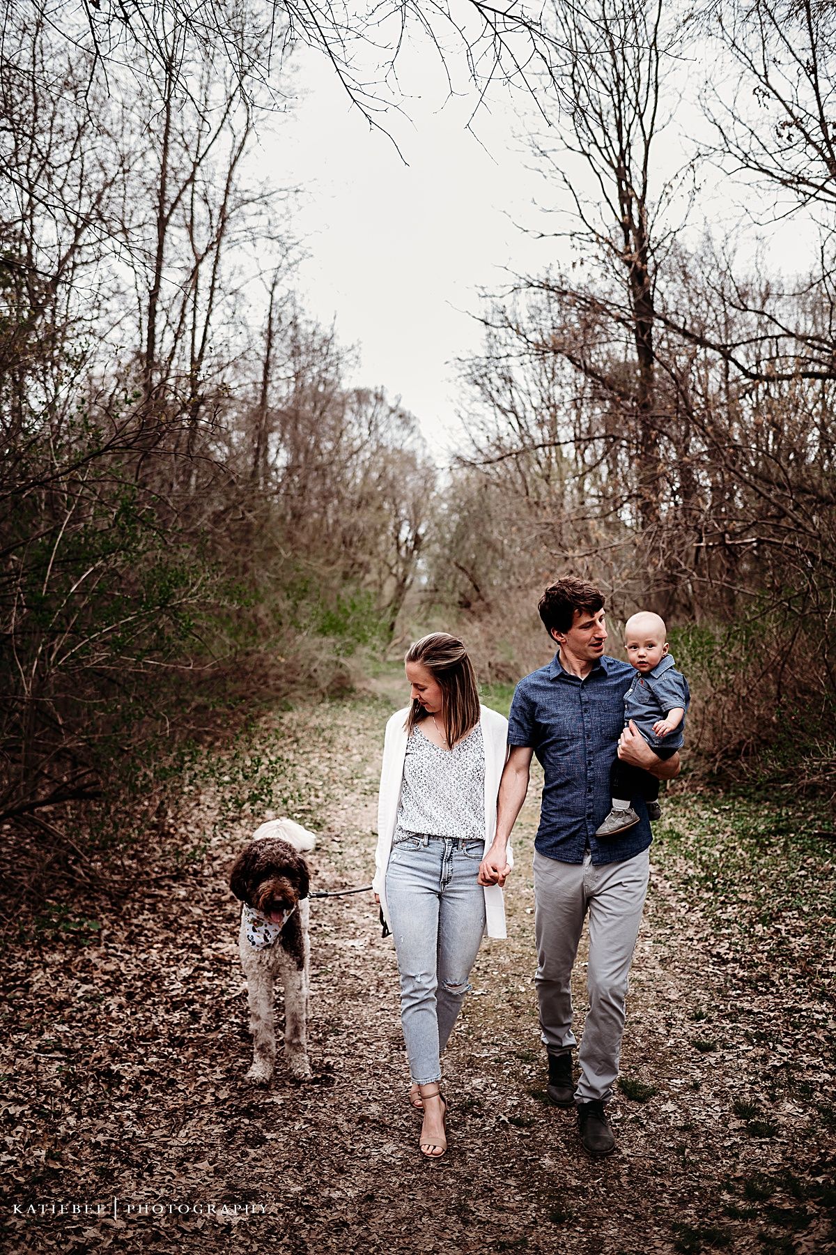 Family takes casual stroll with their dog on wooded path during autumn.