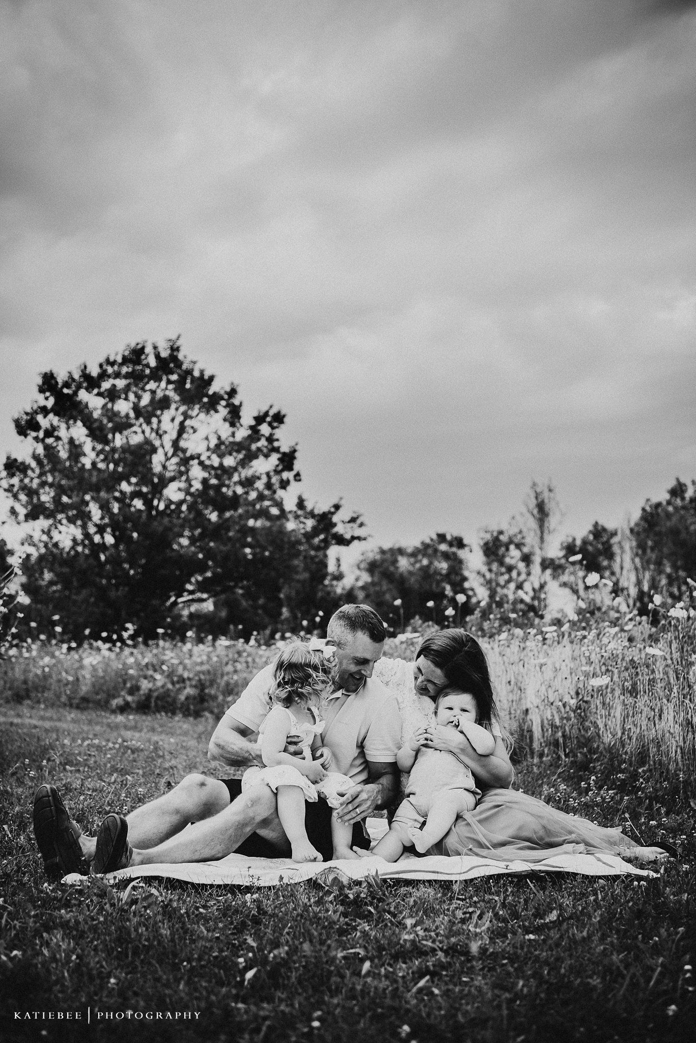 A black and white photo of a family relaxing on a blanket in a meadow.