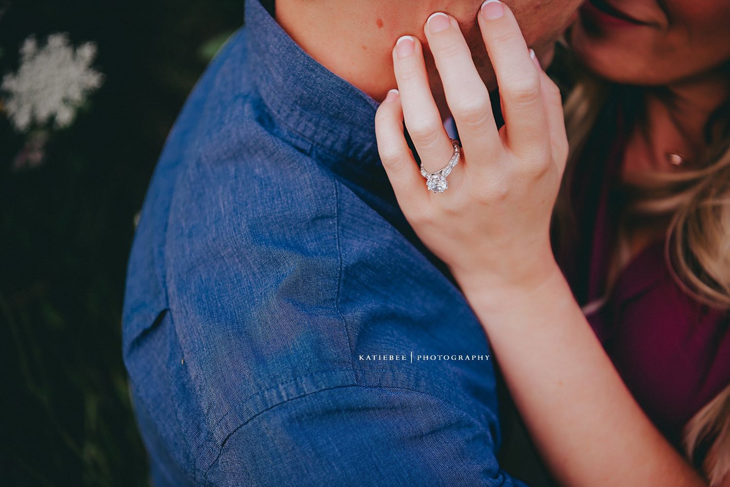 Close up shot of an engagement ring with denim and burgundy clothing.