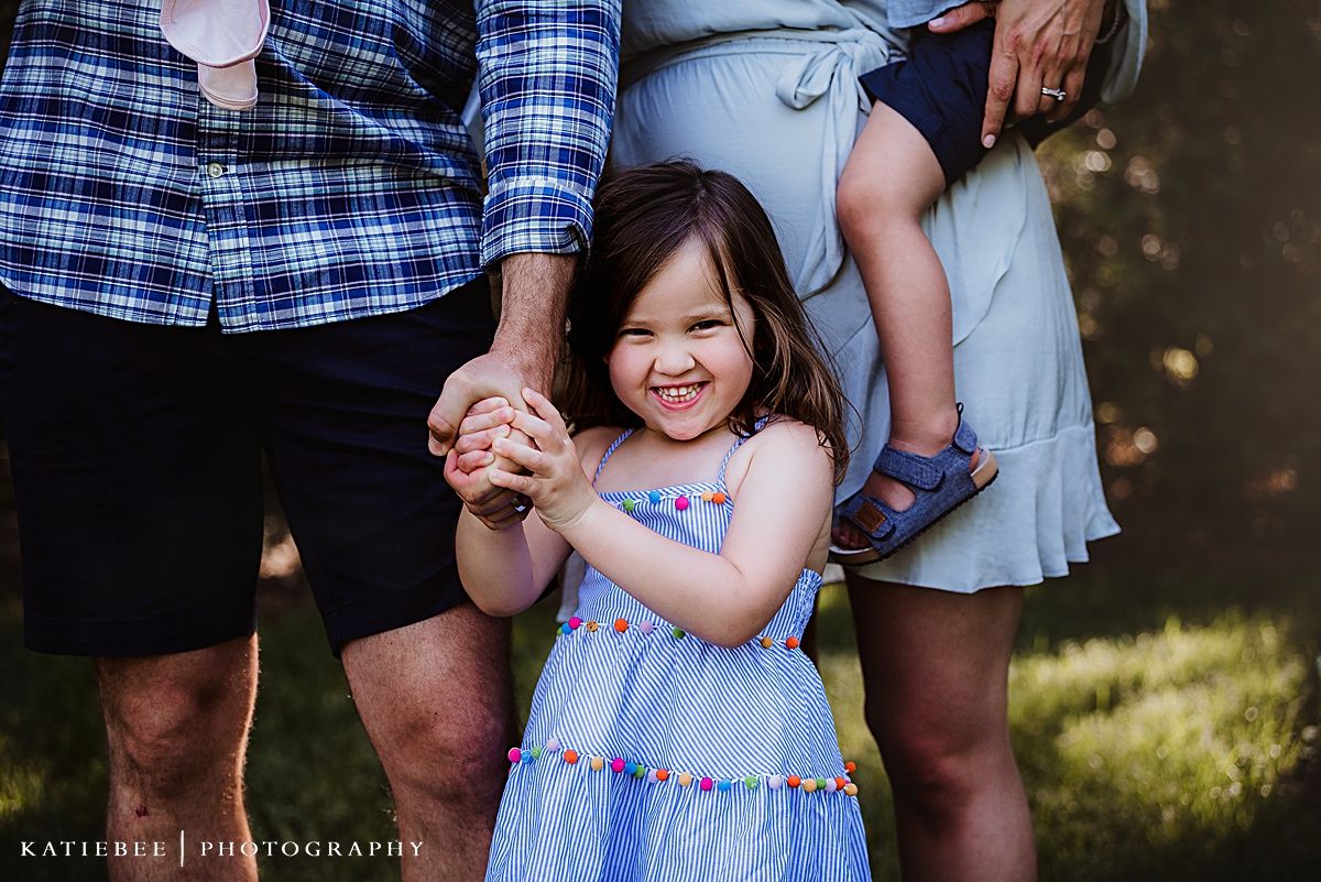 A happy child in a blue dress plays between adults outdoors.