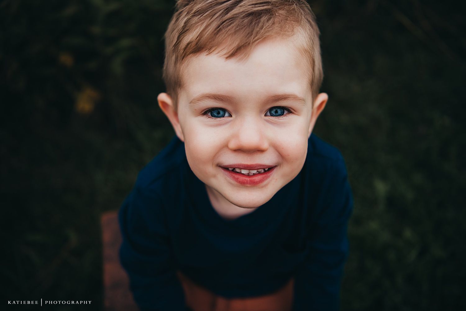 Close up portrait of a smiling child in navy blue against a dark background.