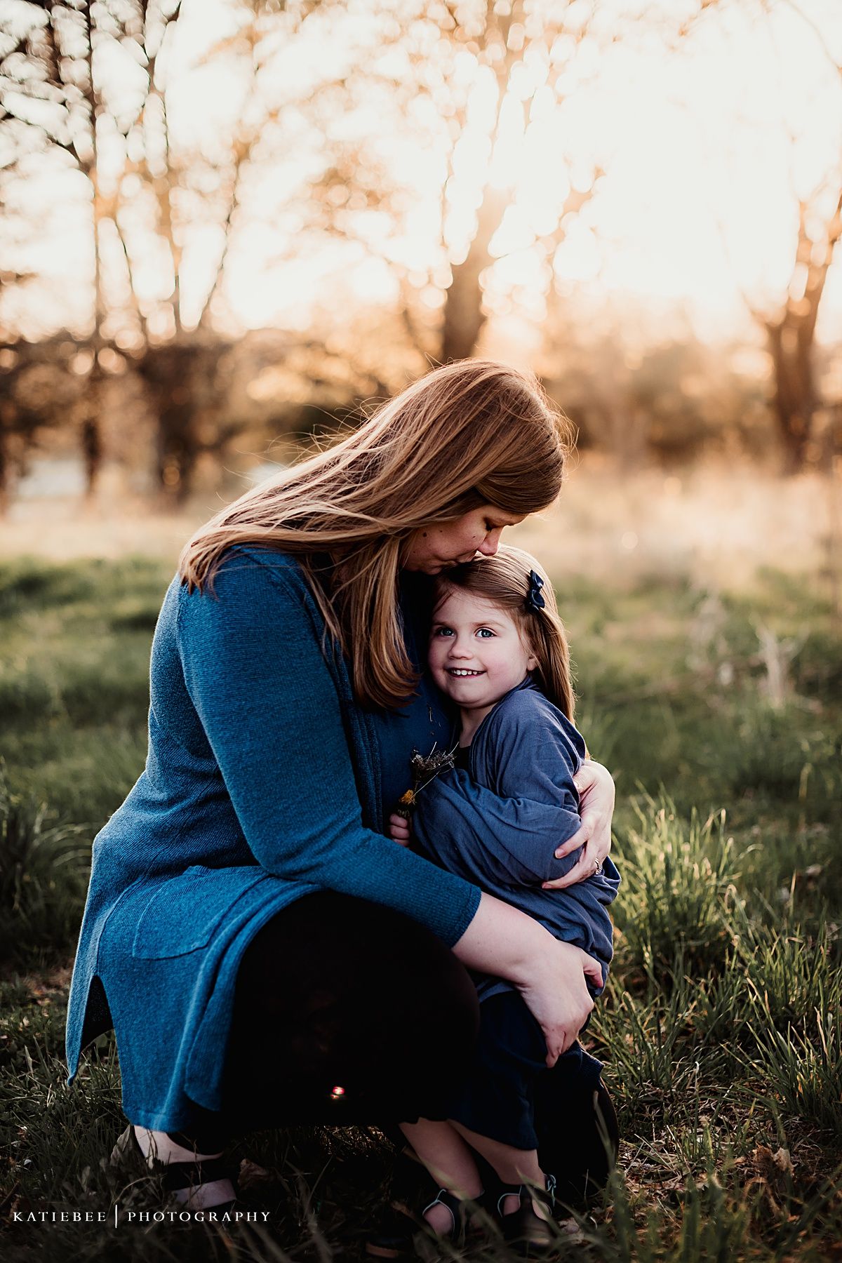 Intimate mother-child portrait captured during golden hour in a grassy field.