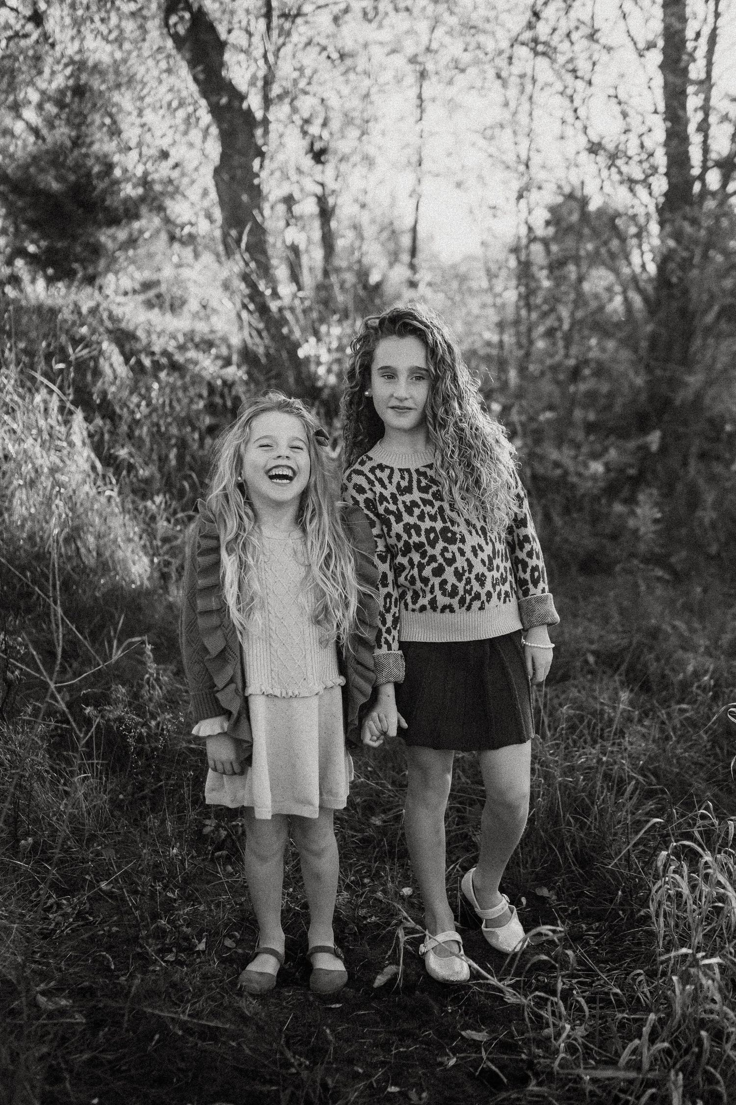 Two children standing together outdoors in a black and white nature setting during autumn.