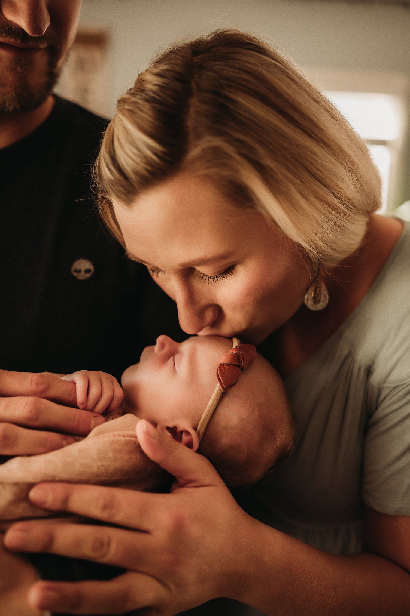 An intimate moment as adults share loving attention with a sleeping infant wrapped in soft fabric.