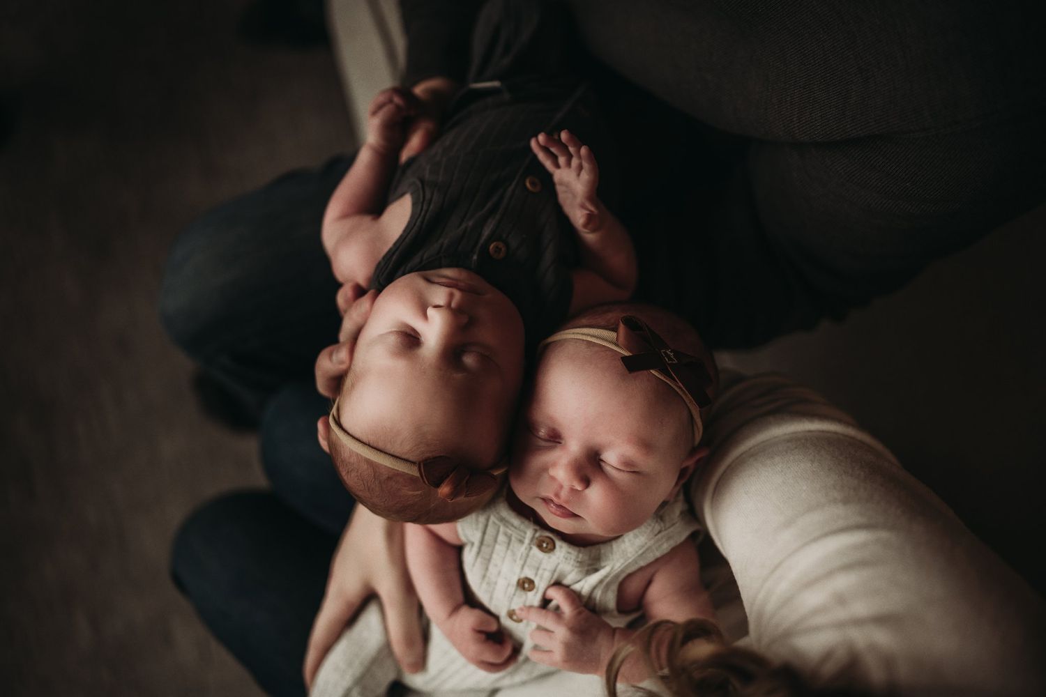 Overhead view of two babies lying together on a dark cushioned surface.