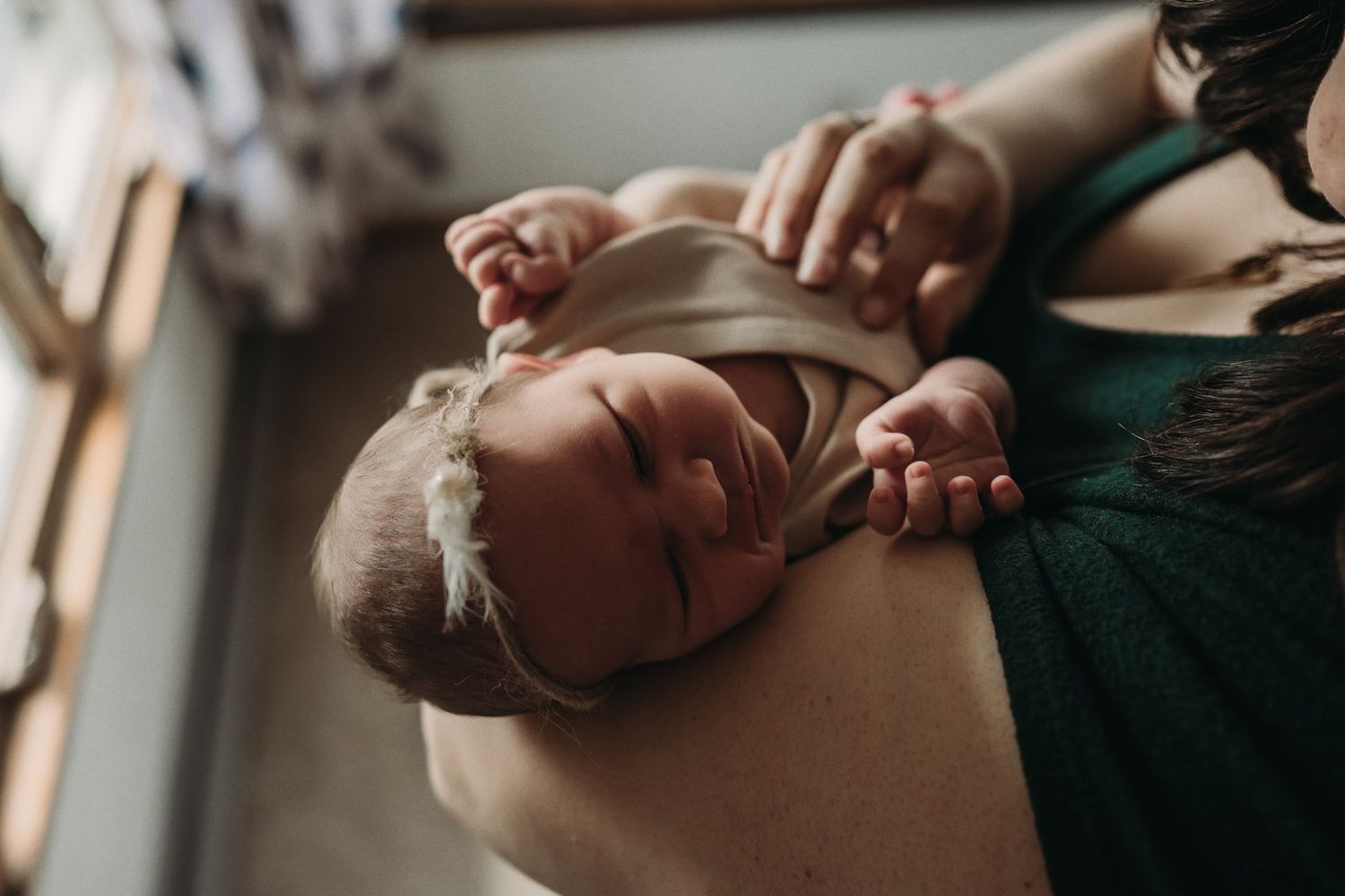 Gentle moment of newborn baby resting on parent's chest near window.