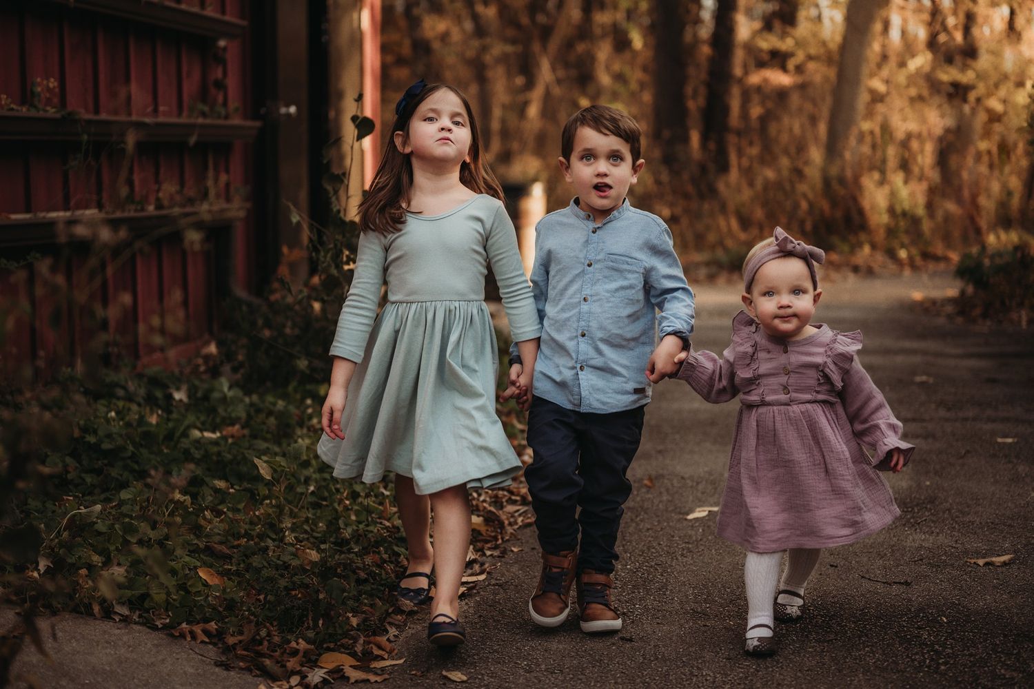 Family walking together on autumn path with red wooden fence and fallen leaves.