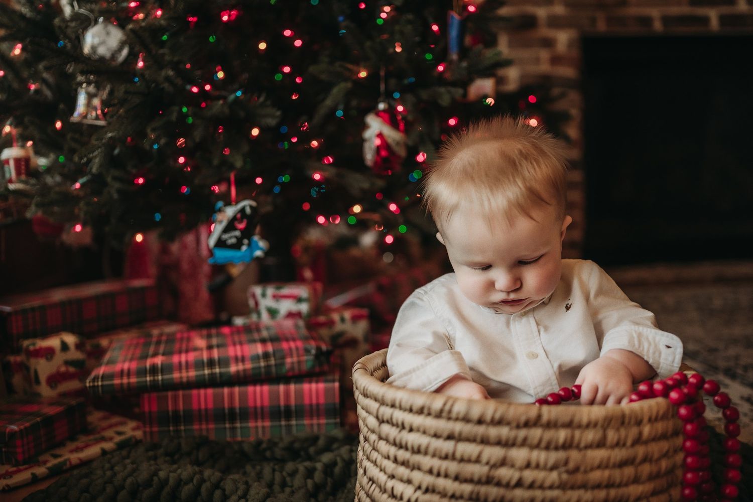 Adorable holiday moment with a small child sitting in a woven basket by a lit Christmas tree.