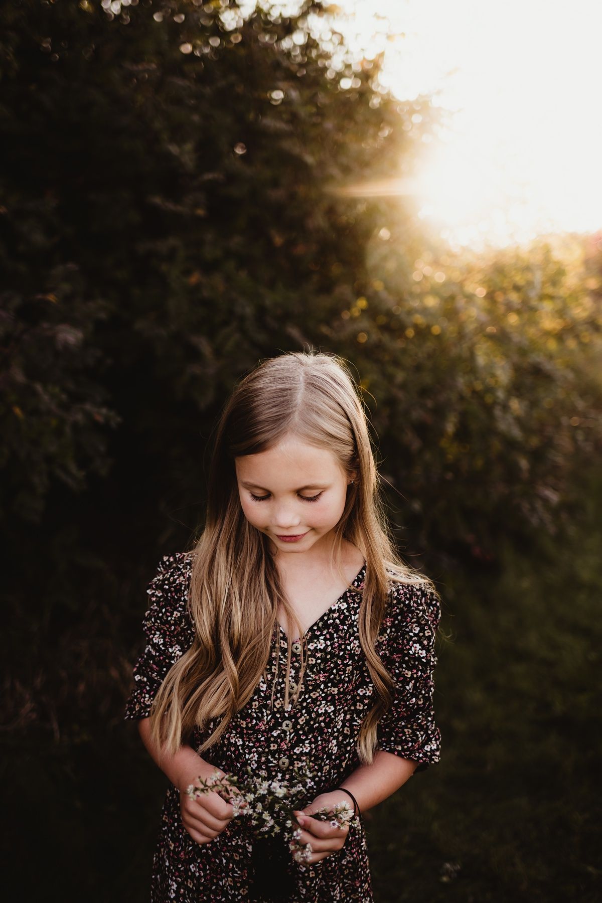 Young person in floral dress looking down thoughtfully at sunset.