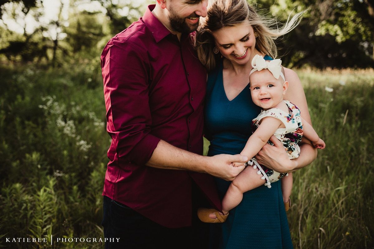 Outdoor family portrait with burgundy and teal clothing against natural greenery.