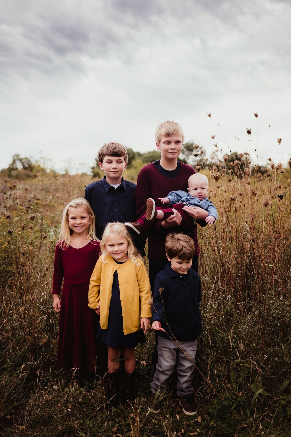Group portrait of children standing among tall wildflowers on an overcast day.