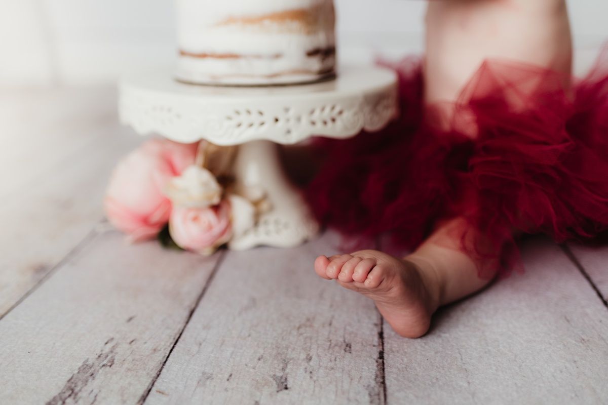 Close up of tiny feet and white cake during first birthday cake smash photo session.