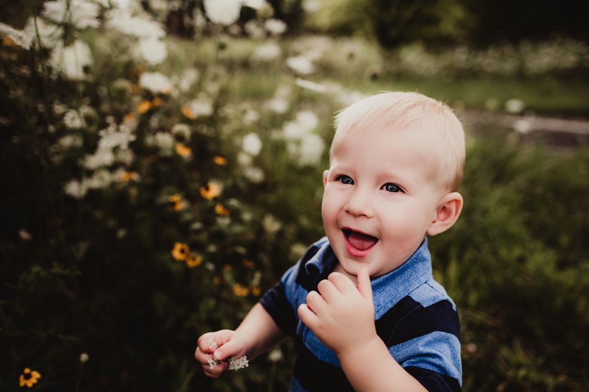 Close-up of a laughing baby in a blue shirt against a natural backdrop.
