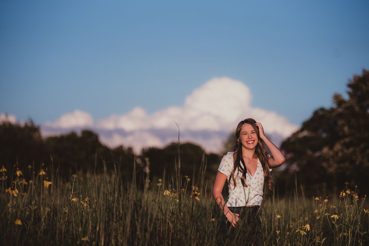A candid summer portrait in a wildflower meadow with puffy clouds.