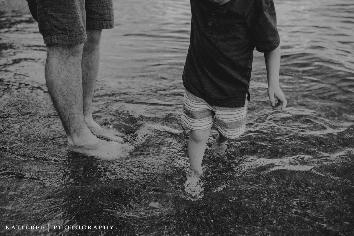 A black and white photo of feet standing in shallow water at the beach.