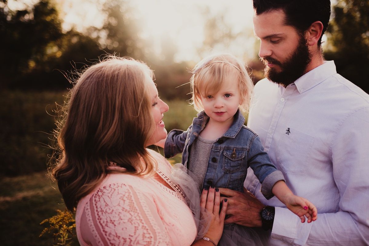 Family portrait at sunset with parents holding their toddler in a field of wildflowers.