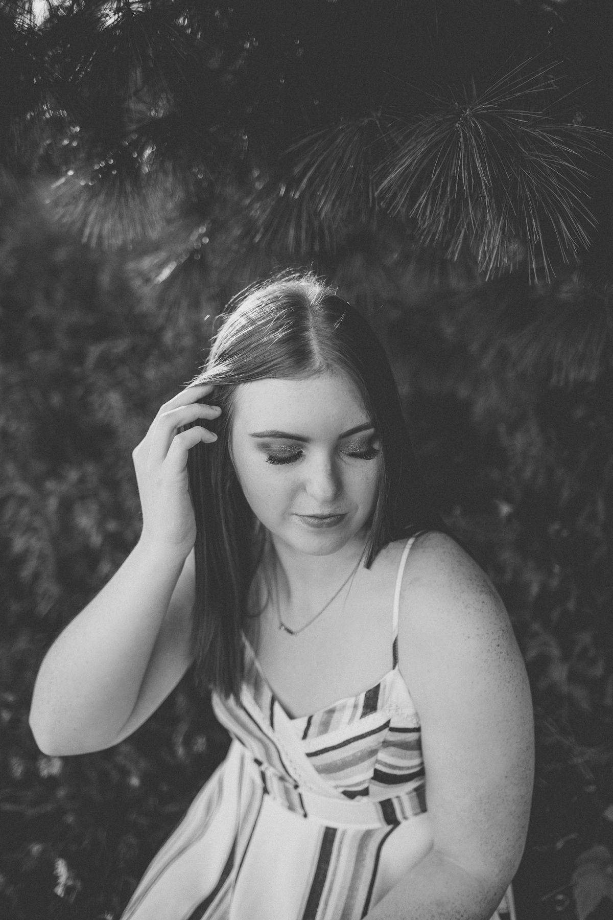 Black and white portrait with soft natural lighting under pine branches.
