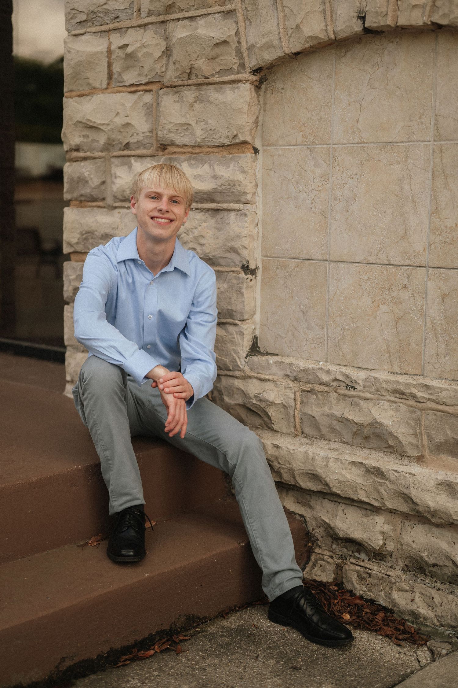 Person in light blue shirt sits casually on stone steps against a textured limestone wall.