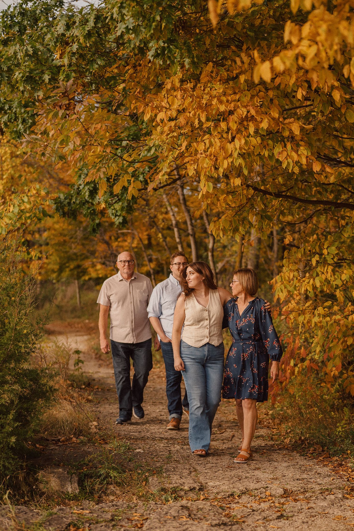 A family takes a stroll together along a wooded trail with beautiful fall foliage creating a golden canopy above.
