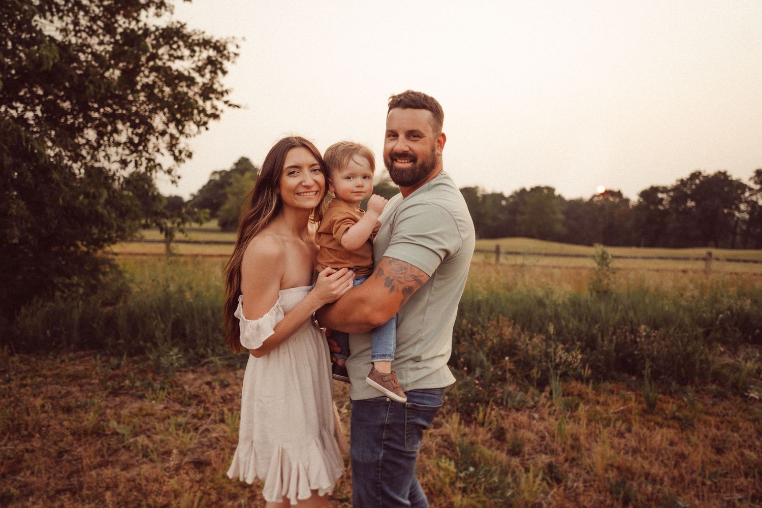 A candid family moment captured during sunset in a rustic field setting.
