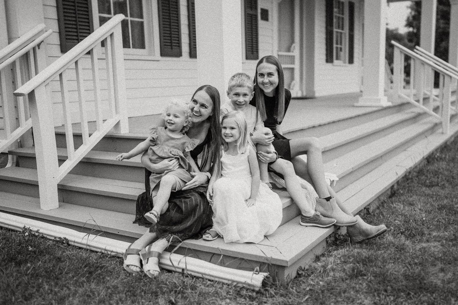 Black and white portrait of a family group sitting together on wooden porch steps.