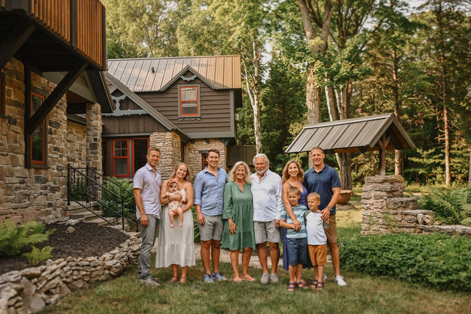 A group photo in front of a rustic stone and wood cottage surrounded by trees.