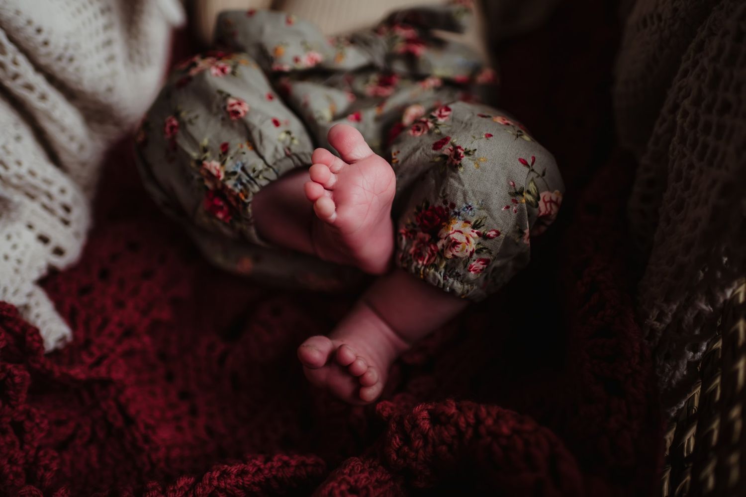 Tiny baby feet resting on floral fabric with red knit blanket.