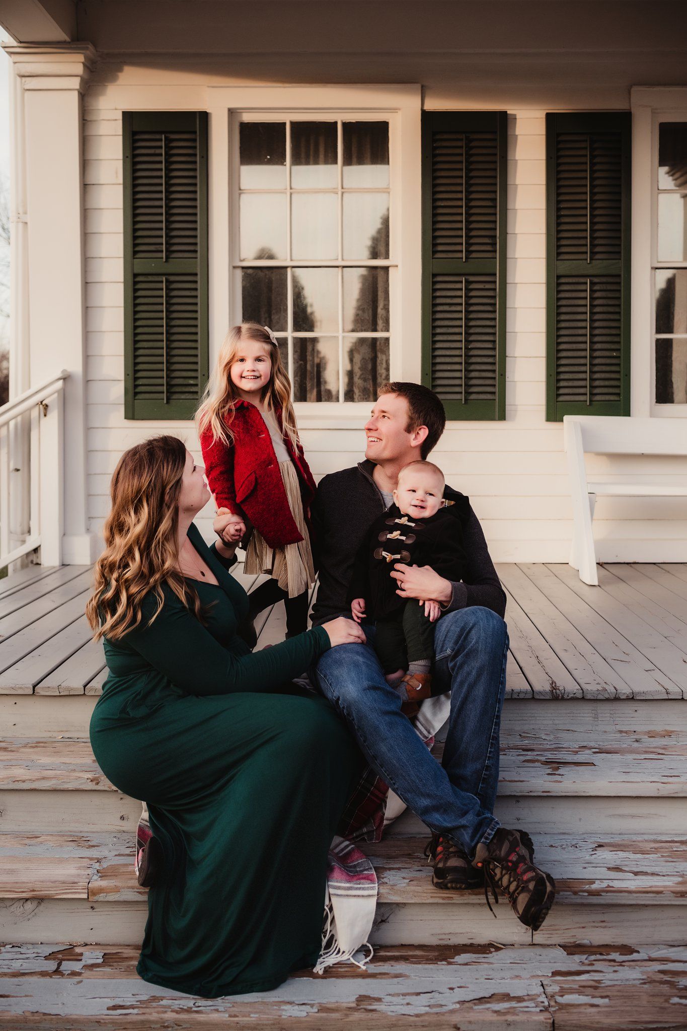 Family portrait session on historic white porch with green shutters during golden hour.
