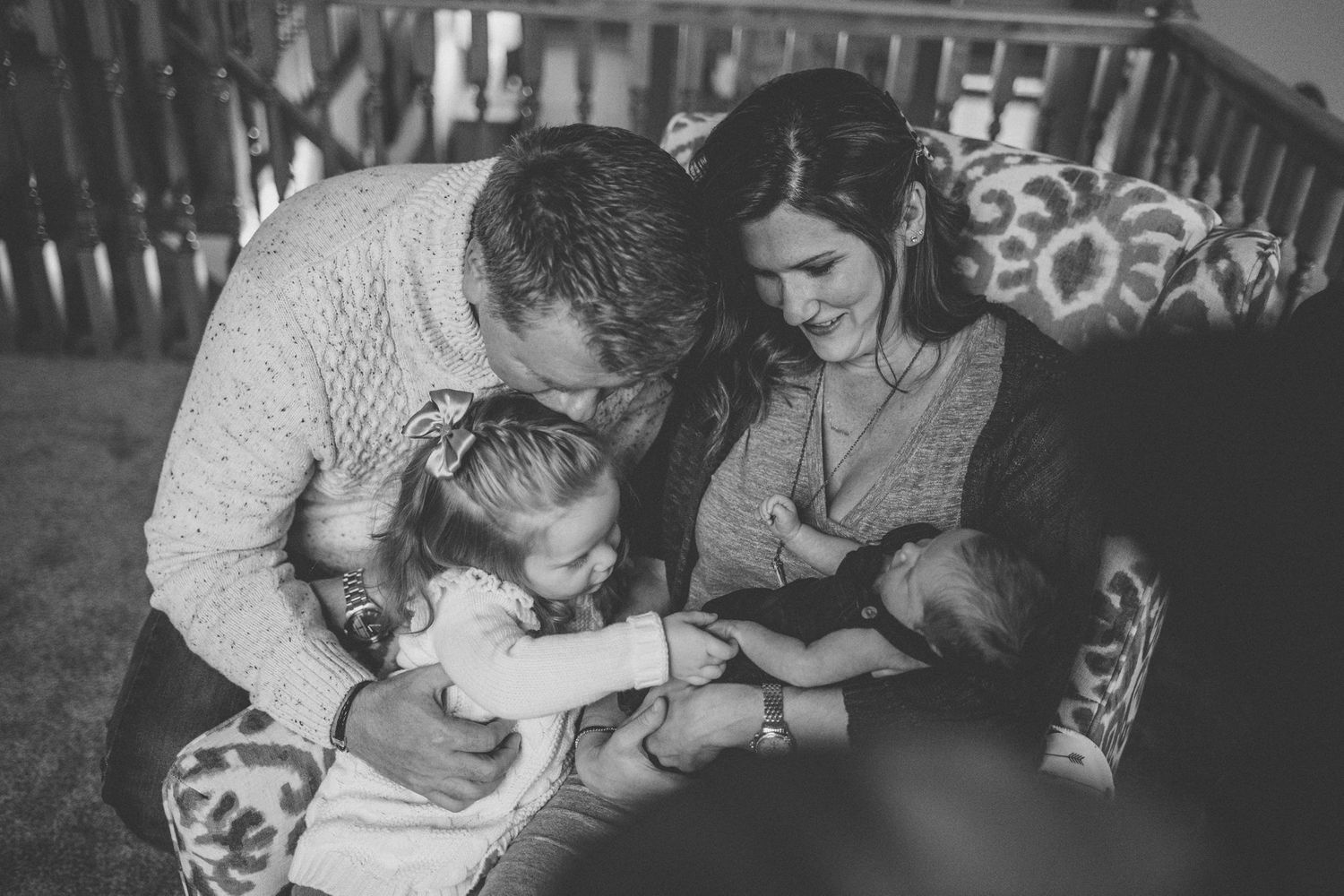 A black and white photo of a family sharing an intimate moment together on a patterned chair.