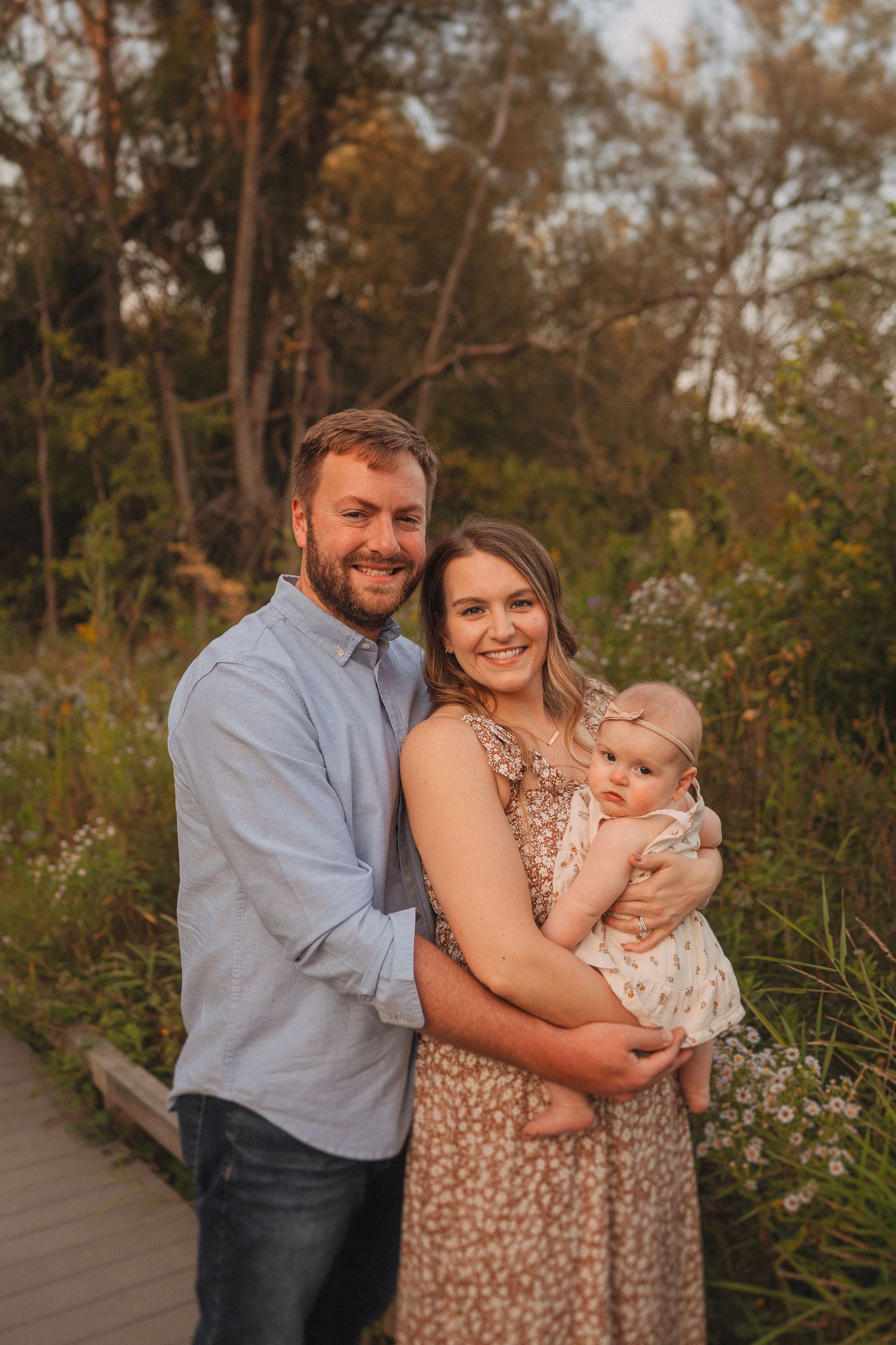 A happy family portrait taken on a wooden boardwalk during golden hour.