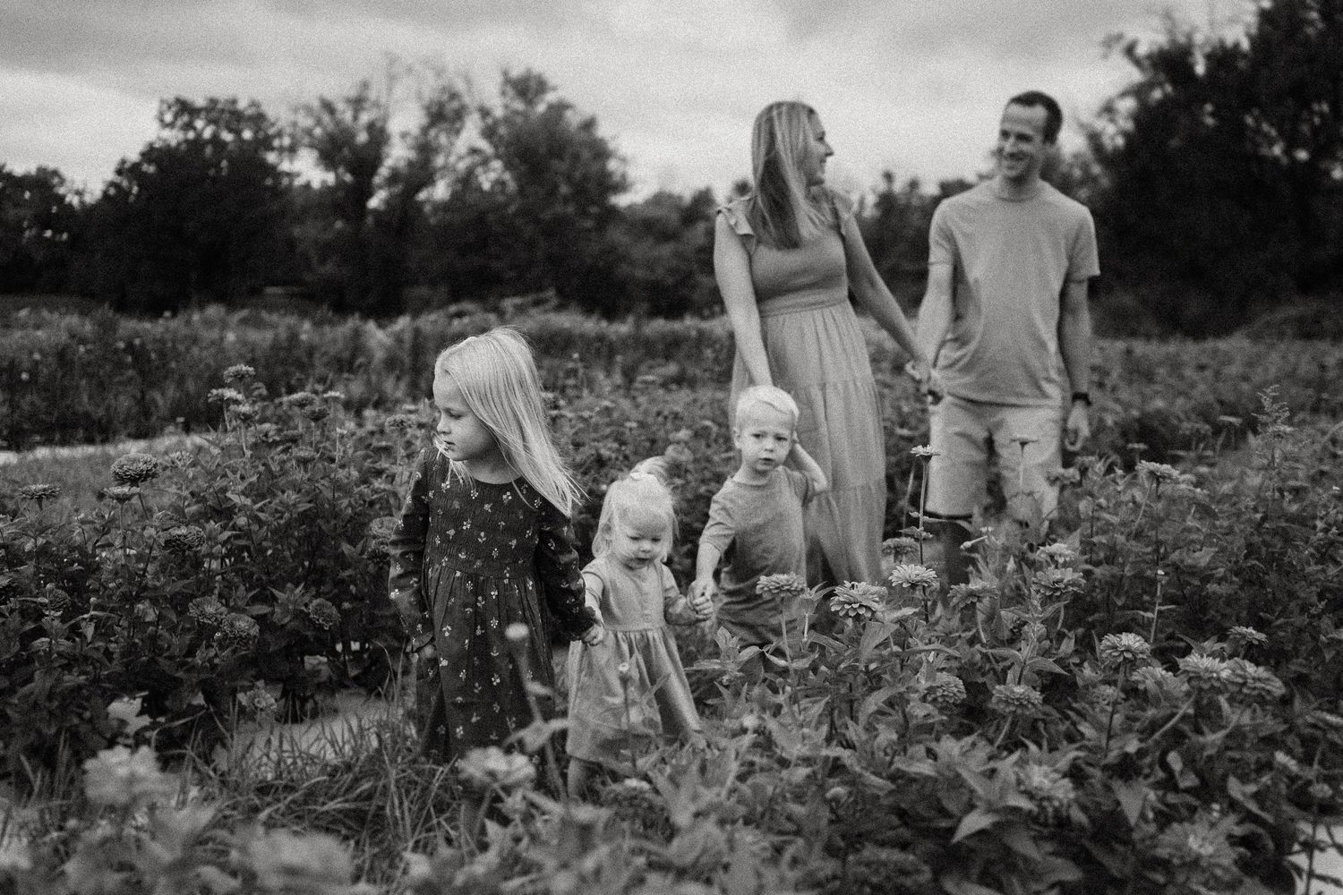 Family exploring together in a lush flower garden on a cloudy day.