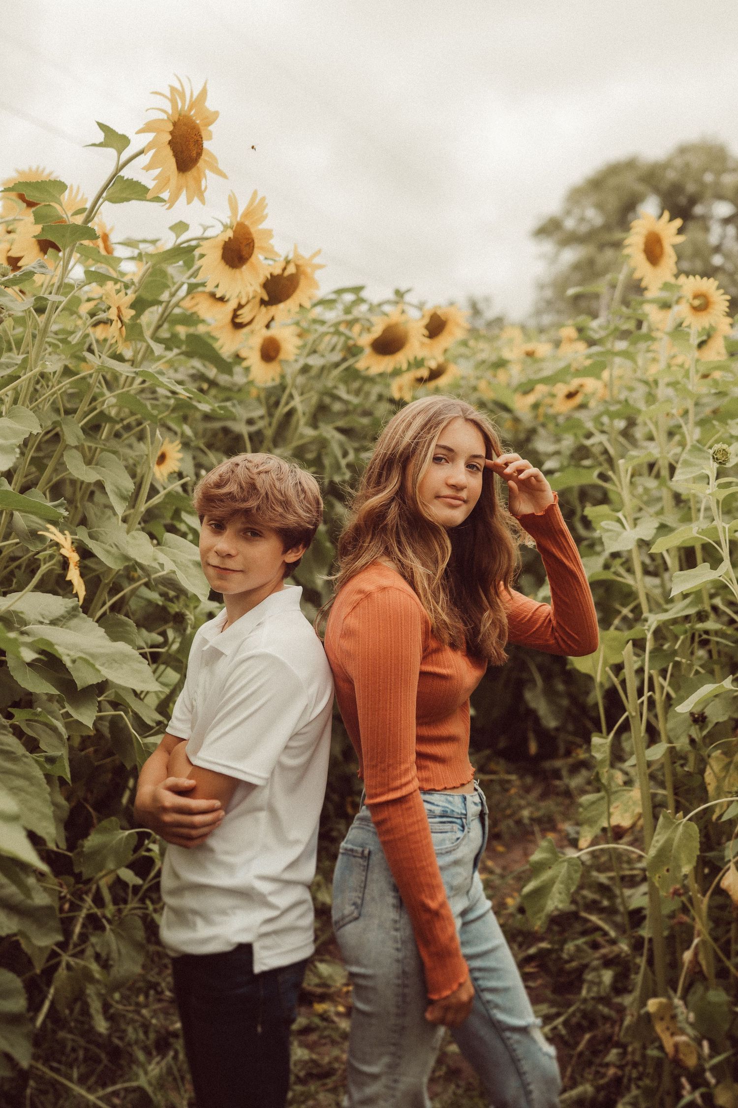 Two people strike playful poses while exploring a sunflower field.